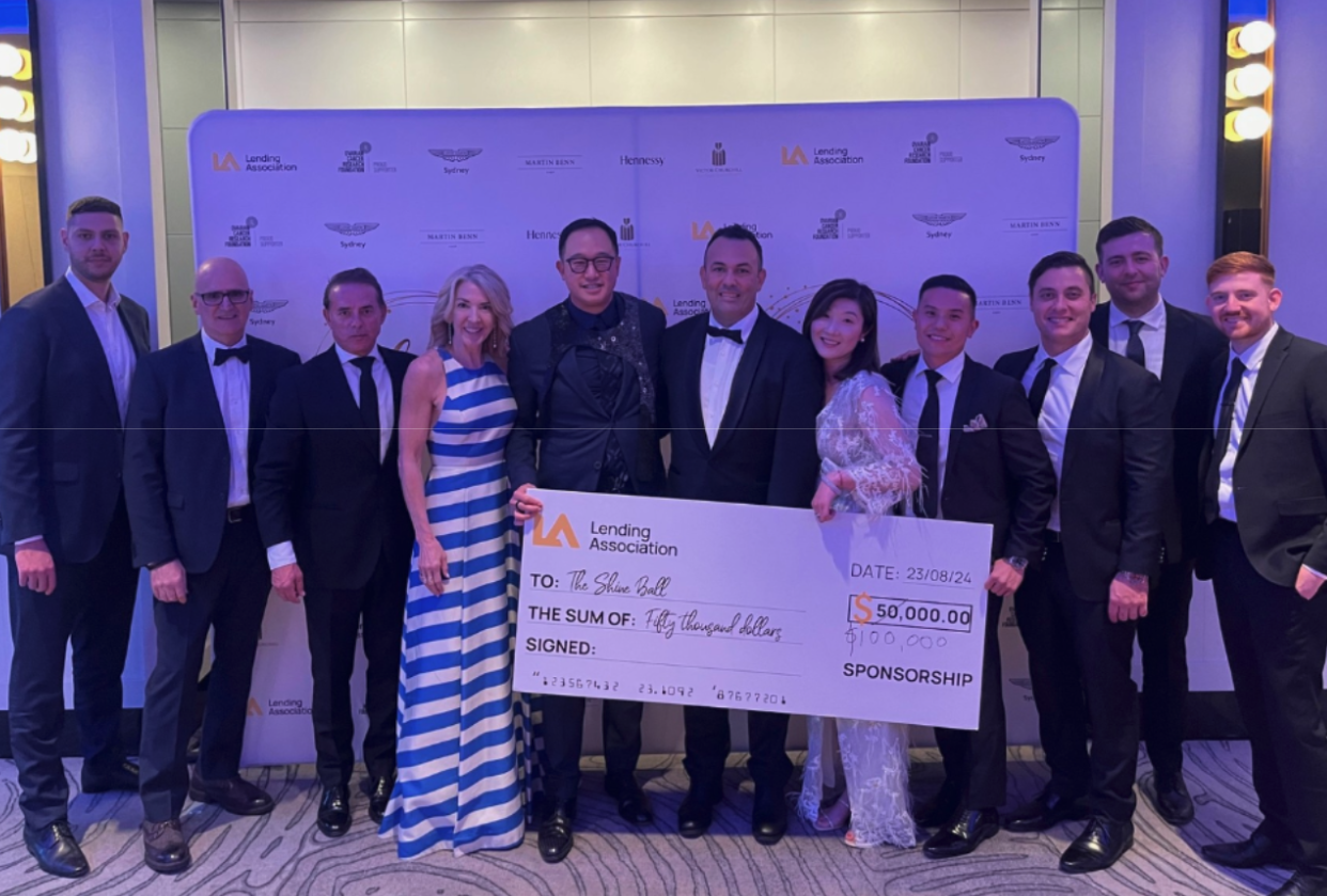 A group of people in formal attire stand together holding a large sponsorship check for $50,000